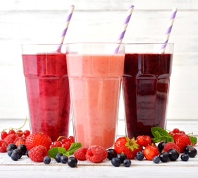 Three glasses of smoothies with different berries on wooden background